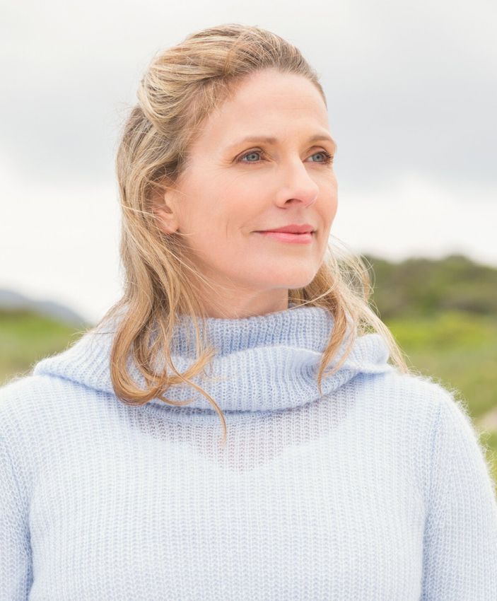 Woman smiling outdoors in soft blue sweater.