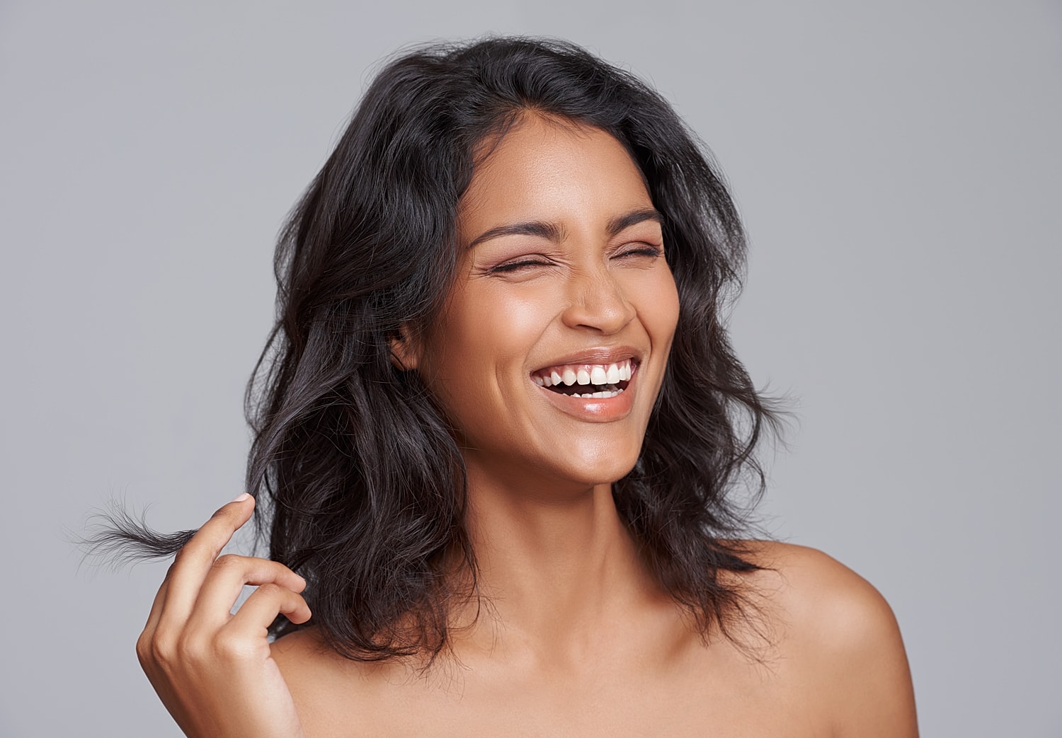 Smiling woman with wavy hair against grey background.